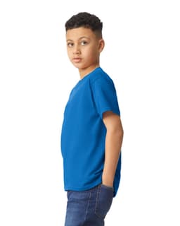 A youth T-shirt in vivid blue, featuring a branded logo, displayed on a model with hands in pockets.