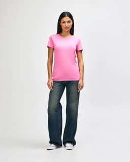 A pink Gildan Heavy Cotton Ladies' T-Shirt worn by a model paired with blue jeans and white sneakers.