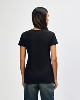 A black Gildan Heavy Cotton Ladies' T-Shirt is displayed from the back, worn with blue jeans. The shirt has a logo.