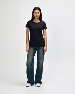 A black ladies' t-shirt displayed on a model, paired with blue jeans and white shoes, featuring a logo.