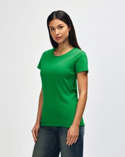 A woman wearing a green Gildan Heavy Cotton ladies' T-shirt, paired with blue jeans against a plain background.