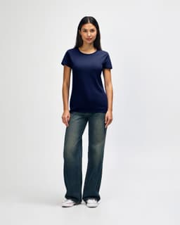 A model wearing a navy blue Gildan Heavy Cotton Ladies' T-Shirt paired with blue jeans and white sneakers.