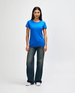 A blue Gildan Heavy Cotton Ladies' T-Shirt displayed on a model, paired with denim jeans and white sneakers.