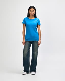 A woman wearing a bright blue Gildan Heavy Cotton Ladies' T-Shirt and jeans, standing against a plain background.