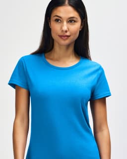 A woman smiles while wearing a bright blue Gildan Heavy Cotton ladies' t-shirt, featuring a logo on the chest.