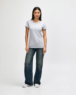 A grey ladies' T-shirt is worn by a model, paired with blue jeans and white sneakers. The shirt features a logo.
