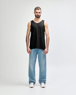 A black Gildan Heavy Cotton adult tank top worn by a model, paired with black trousers and sneakers.