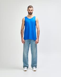A blue tank top displayed on a model wearing black pants and sneakers, featuring a logo.