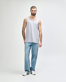 A grey Gildan Heavy Cotton adult tank top displayed on a model, paired with black pants and sneakers.