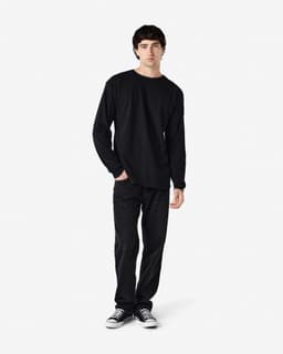 A black long sleeve t-shirt worn by a model, paired with black pants and casual shoes. The shirt has a logo.