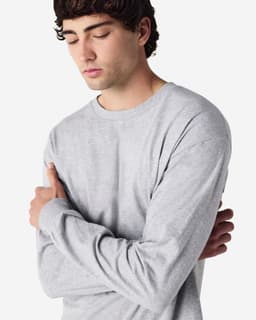 A grey long sleeve T-shirt worn by a model with arms crossed, featuring a simple design and logo.