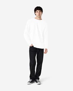 A model wearing a white long sleeve T-shirt with black jeans and sneakers, standing against a light background.