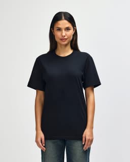 A model wearing a black Gildan Softstyle adult t-shirt paired with light blue jeans. The shirt has a logo.