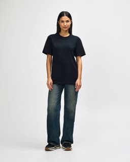 A black Gildan Softstyle adult T-shirt displayed on a model wearing light blue jeans and white shoes, with a plain background.