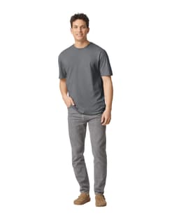 A man stands wearing a grey Gildan Softstyle adult T-shirt paired with light grey jeans and casual footwear.