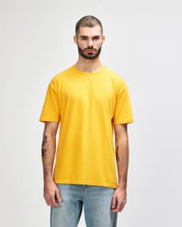 A person stands wearing a bright orange Gildan Softstyle adult T-shirt, paired with grey jeans. The shirt has a logo.