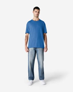 A model wearing a blue Gildan Softstyle adult T-shirt paired with light blue jeans and white shoes.