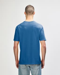 A back view of a man wearing a blue Gildan Softstyle adult t-shirt. The shirt has a logo on the back.