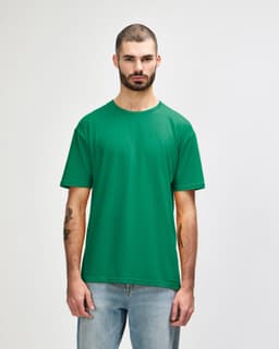 A man wearing a green Gildan Softstyle adult t-shirt, standing against a plain background, paired with blue jeans.