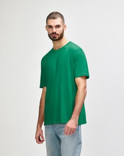 A green Gildan Softstyle adult t-shirt displayed on a model, featuring a simple design and loose fit.