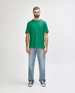 A green Gildan Softstyle adult t-shirt displayed on a male model, paired with light blue jeans.