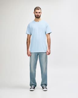 A plain light blue Gildan Softstyle adult T-shirt worn with straight-leg jeans and white shoes, featuring a logo.