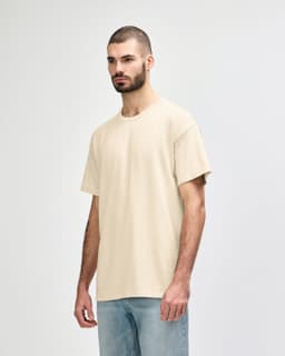 A beige Gildan Softstyle adult T-shirt features a relaxed fit and short sleeves, paired with light blue jeans.