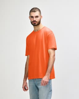 An orange Gildan Softstyle adult T-shirt displayed on a model wearing light blue jeans. The shirt features a logo.