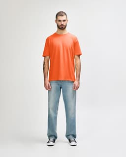 An orange Gildan Softstyle adult T-shirt worn by a man, paired with light blue jeans and white shoes.