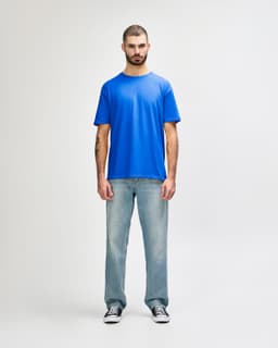 A blue Gildan Softstyle adult T-shirt displayed on a model wearing light blue jeans and white shoes.