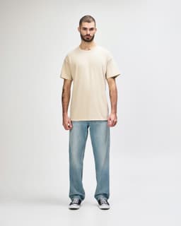 A light beige Gildan Softstyle adult T-shirt displayed on a model, paired with blue jeans. The model stands on a plain background.