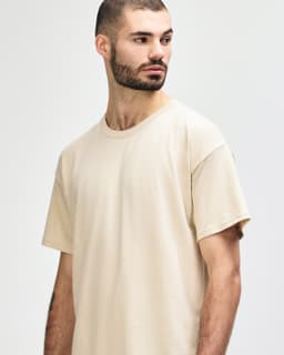A light beige Gildan Softstyle adult T-shirt displayed on a model, featuring a relaxed fit and round neckline.
