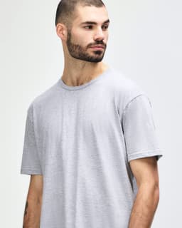 A man stands wearing a grey Gildan Softstyle adult T-shirt and light blue jeans, with a logo on the shirt.