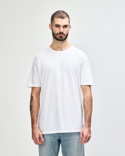 A plain white adult t-shirt is displayed on a model. The t-shirt features a logo and has a relaxed fit.