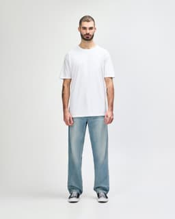 A man stands wearing a plain white Gildan Softstyle adult T-shirt paired with light blue jeans.