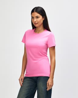 A pink Gildan Softstyle ladies' T-shirt is displayed on a model, styled with denim jeans. The shirt features a logo.