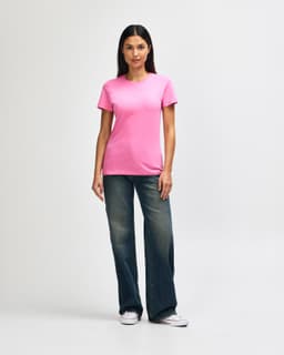 A pink Gildan Softstyle ladies' t-shirt paired with blue jeans and white sneakers, featuring a logo.