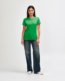 A green Gildan Softstyle ladies' t-shirt paired with blue jeans and white sneakers, modelled by a woman.
