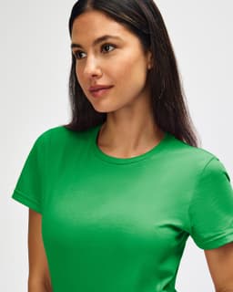 A green Gildan Softstyle ladies' t-shirt displayed on a model with long hair. The shirt has a logo on it.