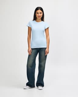 A light blue ladies' t-shirt paired with blue jeans and white sneakers, featuring a brand logo.