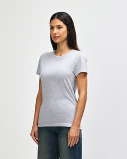 A grey Gildan Softstyle ladies' T-shirt, featured on a model, styled with blue jeans. The shirt has a logo.