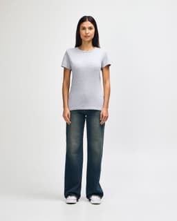 A grey ladies' t-shirt is worn with blue jeans and white sneakers, showcasing a casual outfit. The t-shirt has a logo.