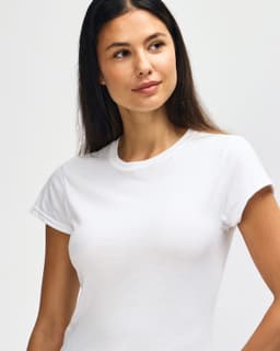 A white Gildan Softstyle ladies' T-shirt displayed on a model with a relaxed pose and a slight smile.
