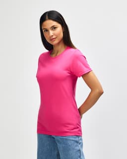 A pink Gildan Softstyle ladies midweight t-shirt displayed on a model, wearing blue jeans, with a plain background.