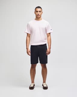 A man wearing a pink t-shirt and black cotton gym shorts, featuring a logo on the shorts.