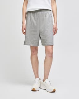 Grey cotton gym shorts with an elastic waistband, worn by a person standing in white shoes. Features a logo.