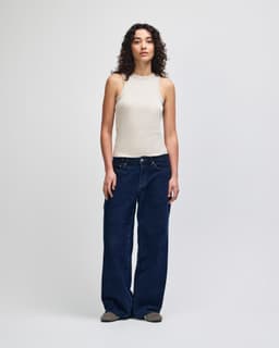 A fitted tank in beige worn with wide-leg denim jeans, featuring a model against a plain background.