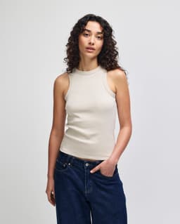 A fitted tank top in a neutral beige colour, worn by a model with curly hair, paired with blue jeans.