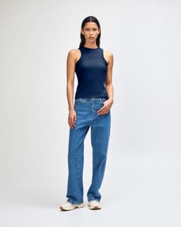 A fitted tank top in navy blue, paired with blue jeans, modelled by a woman standing against a plain background.