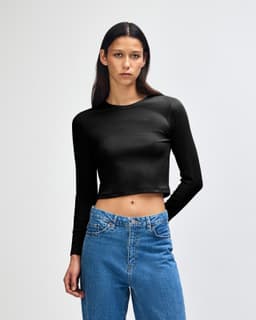 A black long-sleeve crop fitted t-shirt on a model, paired with blue jeans. The shirt features a logo.